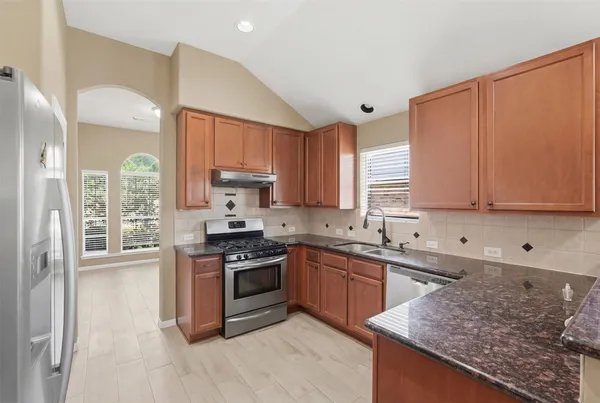 a kitchen with stainless steel appliances granite countertop a stove top oven a sink dishwasher and a refrigerator with wooden floor