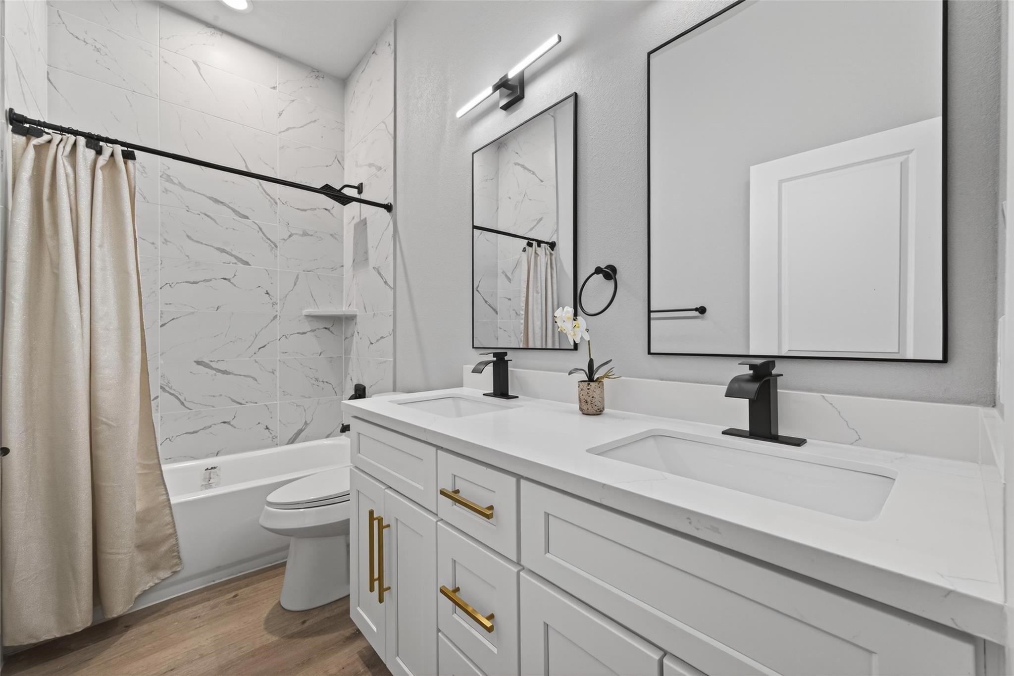 4115 Yale Street Houston, TX 77018 - Photo 28 of 35 Spa-inspired secondary bathroom with dual-sink quartz vanity, custom cabinetry with brushed gold hardware, matte black fixtures, LED vanity lighting, and full-height marble-look tile surround.