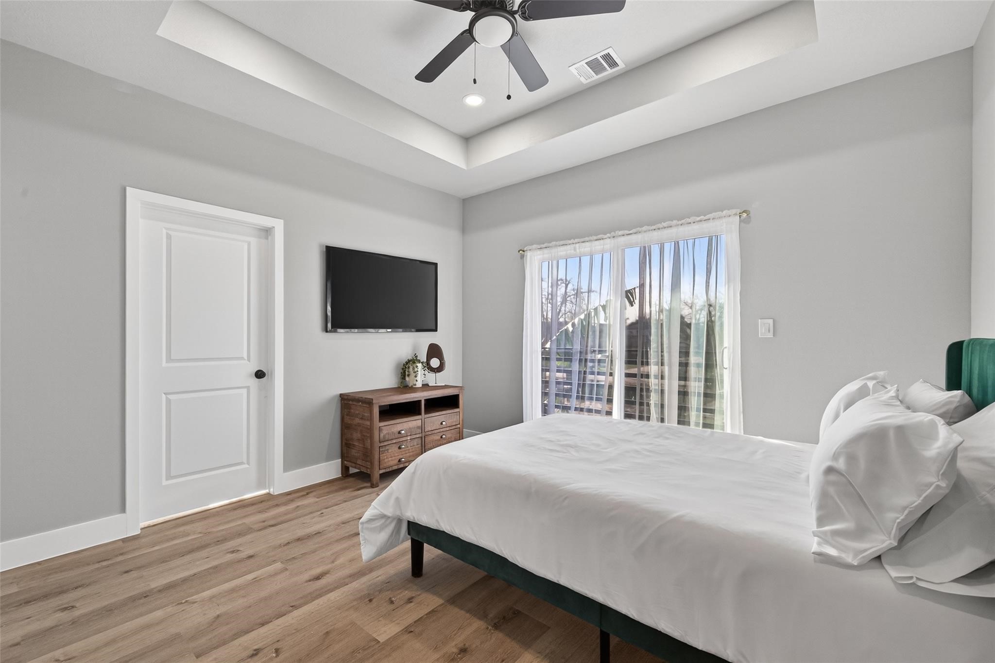 4115 Yale Street Houston, TX 77018 - Photo 30 of 35 Serene primary suite featuring tray ceiling with recessed lighting, ceiling fan, white oak–finish plank laminate flooring, and private balcony access for seamless indoor-outdoor living.