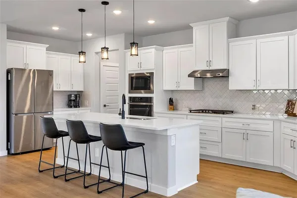 a kitchen with stainless steel appliances a refrigerator a stove a sink and white cabinets with wooden floor