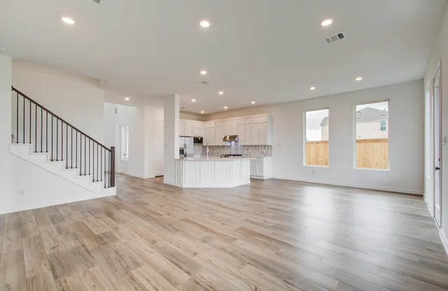 a view of an empty room and kitchen with wooden floor