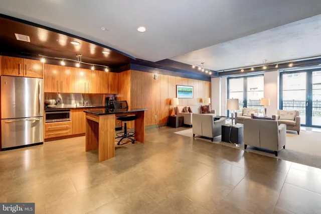 a kitchen with stainless steel appliances kitchen island granite countertop a refrigerator a stove a dining table and chairs with wooden floor