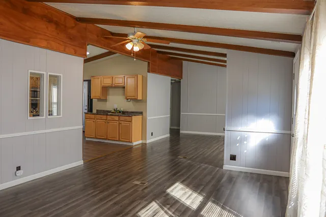a view of empty room with wooden floor and kitchen view