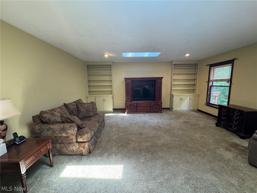 8201 Orchard Road Painesville, OH 44077 - Photo 17 of 45 Spacious room featuring carpet flooring, built-in shelving with lower cabinetry, a prominent window with blinds, and a skylight