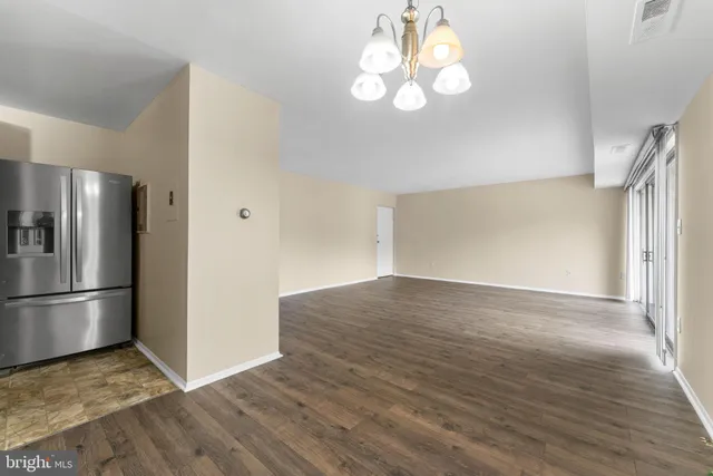 a view of empty room with wooden floor and kitchen