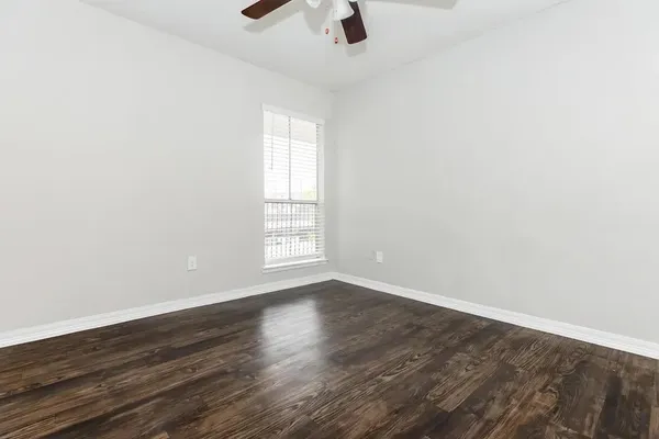an empty room with wooden floor chandelier fan and windows
