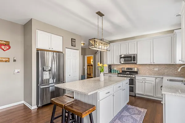 a kitchen with stainless steel appliances a stove a sink dishwasher a refrigerator white cabinets and wooden floor