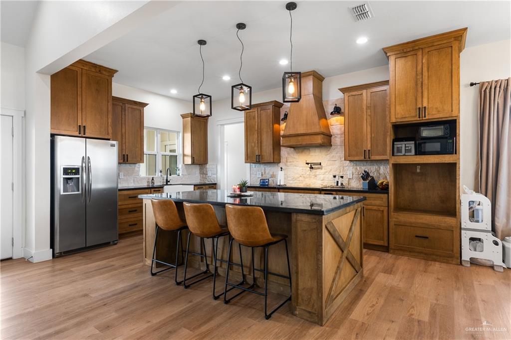 23588 Beefmaster Road Monte Alto, TX 78538 - Photo 8 of 45 a kitchen with stainless steel appliances kitchen island granite countertop a refrigerator a stove a sink and white cabinets with wooden floor