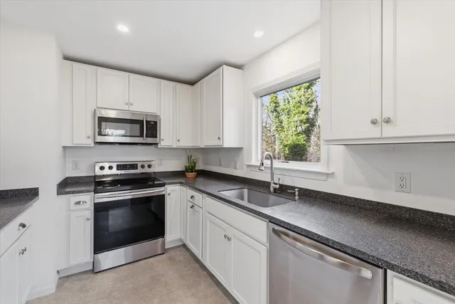a kitchen with granite countertop white cabinets appliances a window and a sink