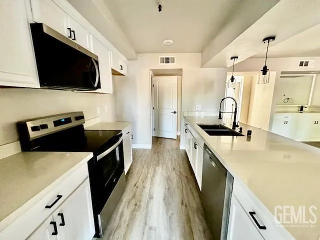 a kitchen with stainless steel appliances a stove top oven a sink a refrigerator white cabinets and wooden floor