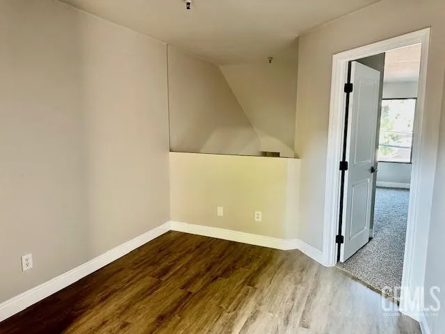 a view of an empty room with wooden floor and a bathroom