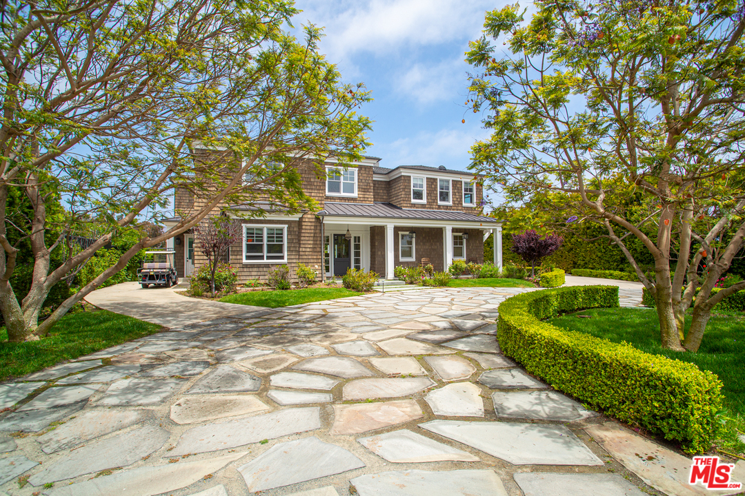 a view of a brick house with a big yard plants and large tree