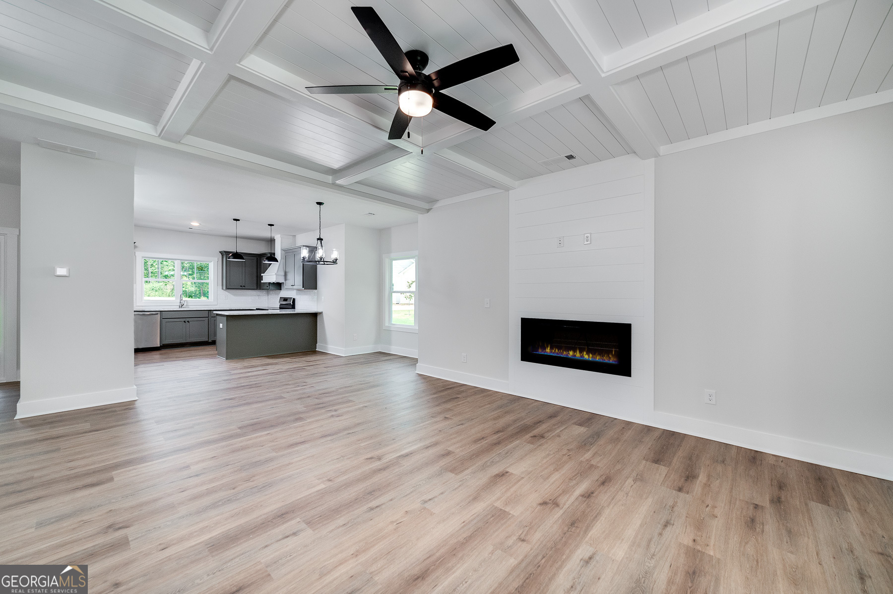 70 Lloyd Street Monticello, GA 31064 - Photo 8 of 16 an empty room with wooden floor a ceiling fan a kitchen with a fireplace and wooden floor