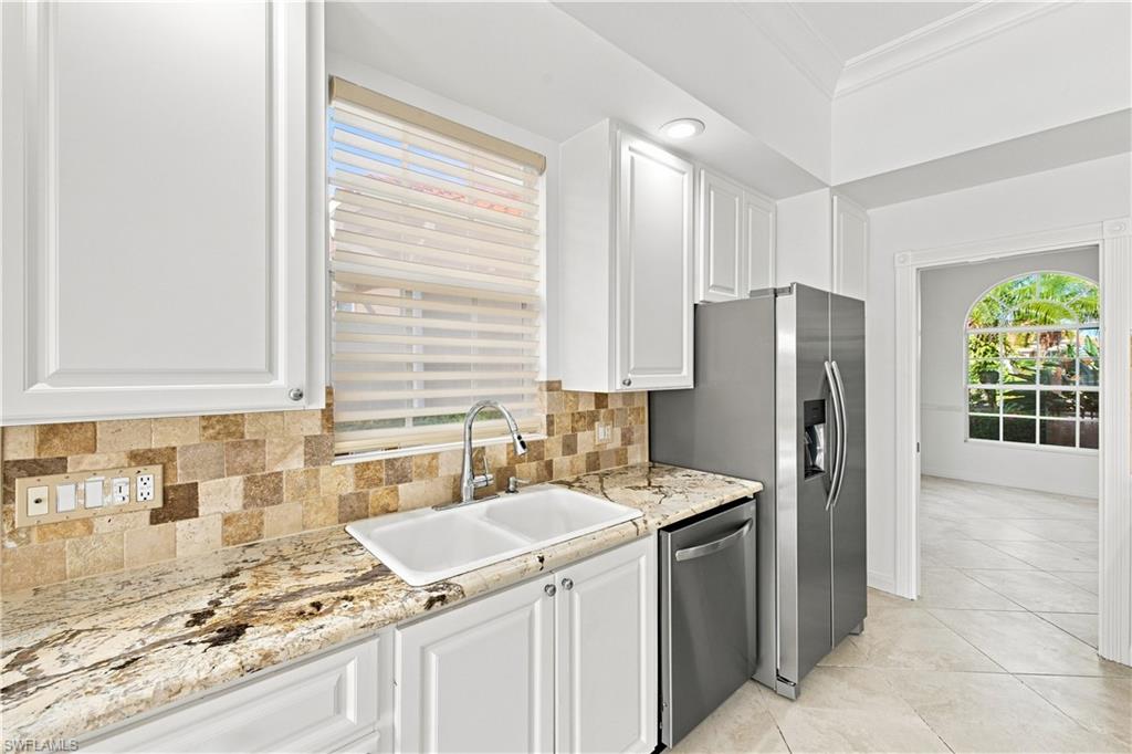 4470 Novato Court Naples, FL 34109 - Photo 5 of 33 White cabinetry, stone tile backsplash, patterned countertops, stainless steel appliances, and arched doorway