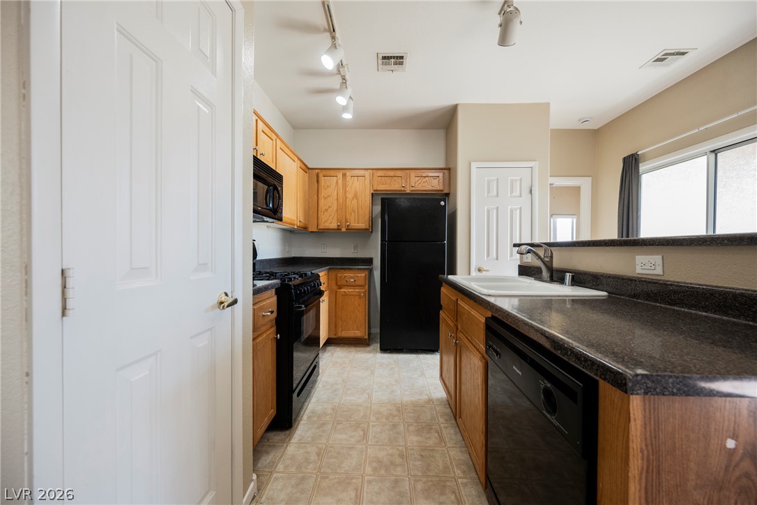 6320 Snap Ridge Street, Unit 201 North Las Vegas, NV 89081 - Photo 3 of 56 A compact kitchen with ample wooden cabinetry and a full suite of black appliances.