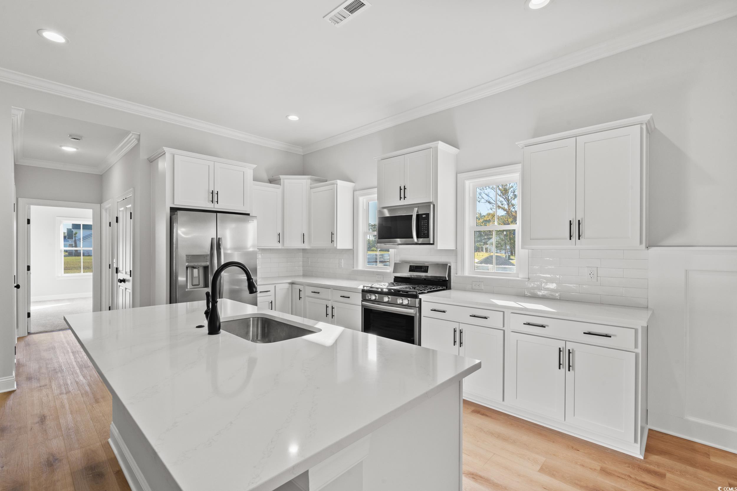 1127 Crooked Hook Road North Myrtle Beach, SC 29582 - Photo 16 of 32 Kitchen featuring white cabinetry, stainless steel appliances, light wood-style floors, crown molding, and an island with sink