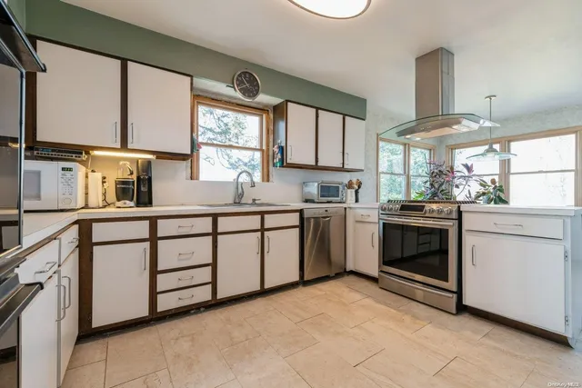a kitchen with white cabinets appliances a sink and a window