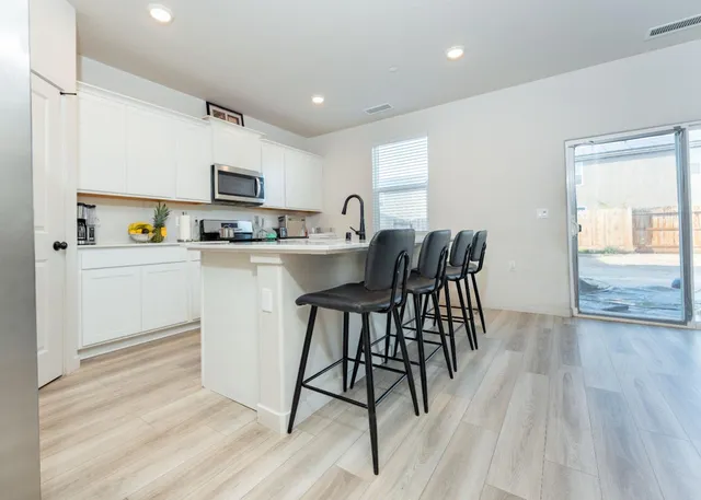 a kitchen with stainless steel appliances granite countertop a stove top oven a sink a dining table and chairs with wooden floor