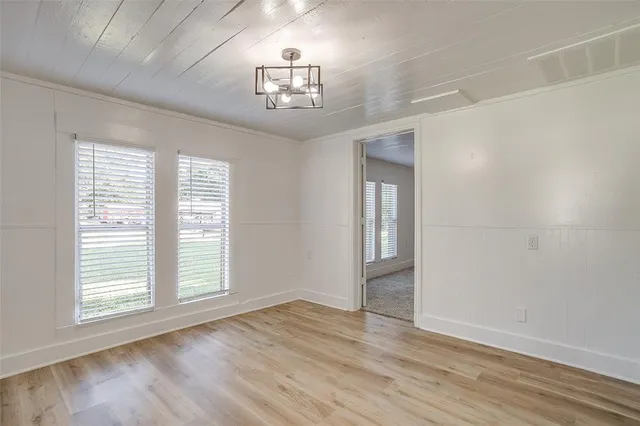 an empty room with wooden floor chandelier and windows