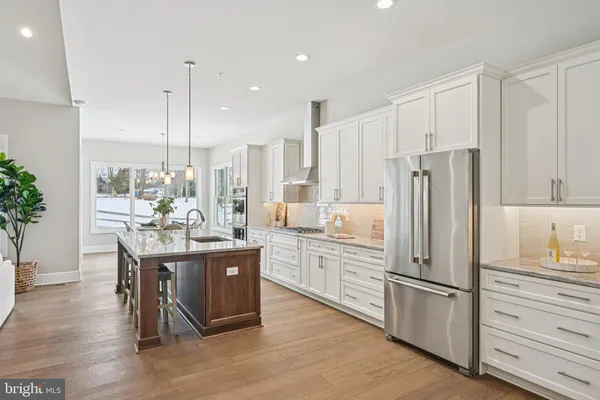a kitchen with stainless steel appliances granite countertop a refrigerator a sink dishwasher a stove and white cabinets with wooden floor