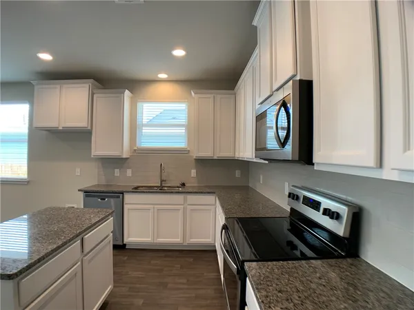 a kitchen with granite countertop a sink a stove and cabinets