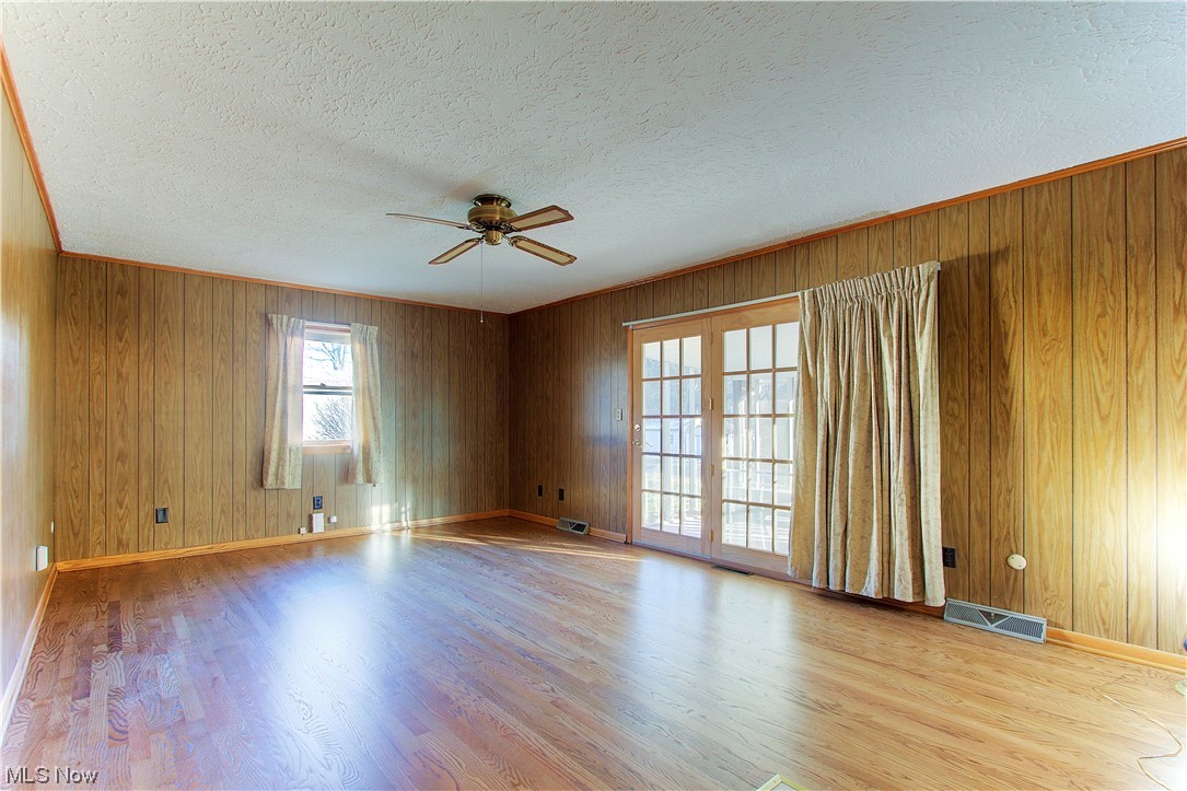 1998 Bridger Road Akron, OH 44312 - Photo 5 of 32 Empty room featuring light hardwood / wood-style flooring, wood walls, ceiling fan, and a textured ceiling