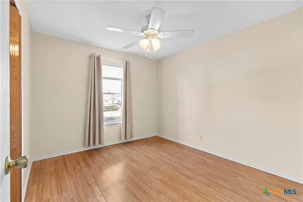 an empty room with wooden floor chandelier fan and windows