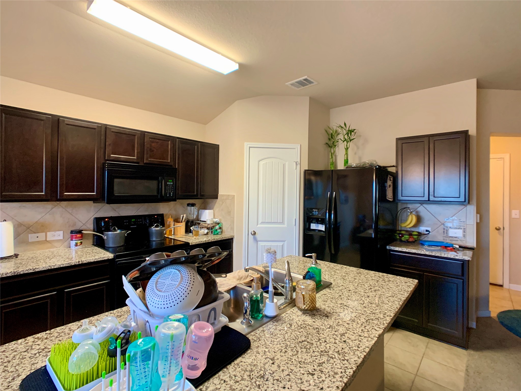 5721 Roderick Drive Austin, TX 78724 - Photo 23 of 26 Kitchen featuring decorative backsplash, dark wood finish cabinetry, black appliances, and light stone countertops