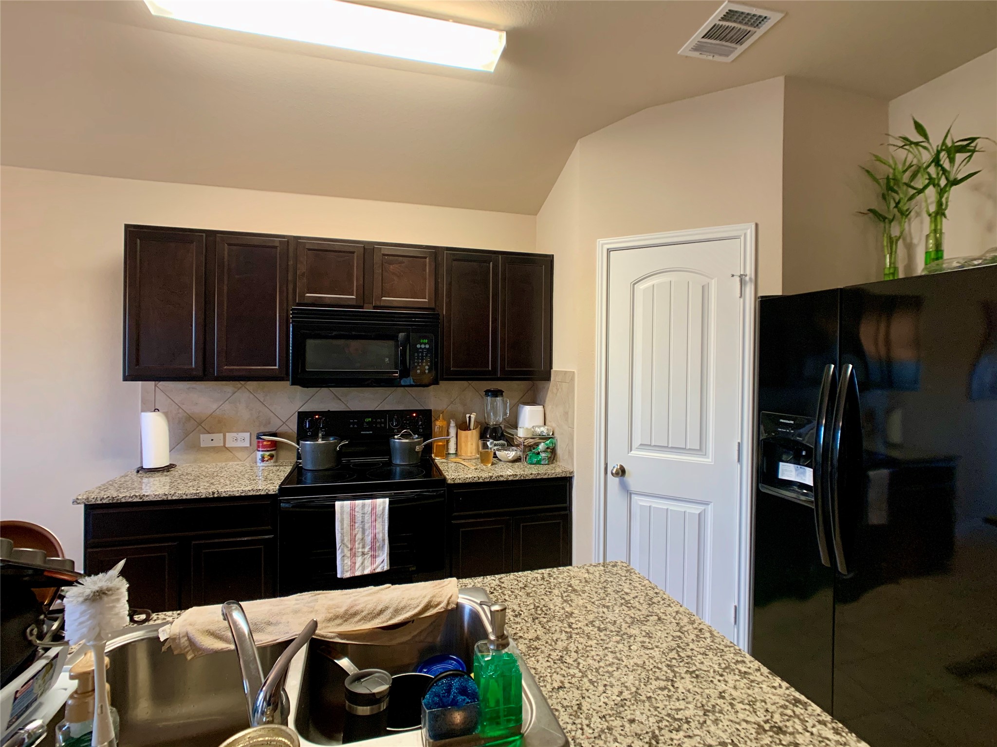 5721 Roderick Drive Austin, TX 78724 - Photo 24 of 26 Kitchen with dark wood finish cabinets, black appliances, light stone countertops, and decorative backsplash