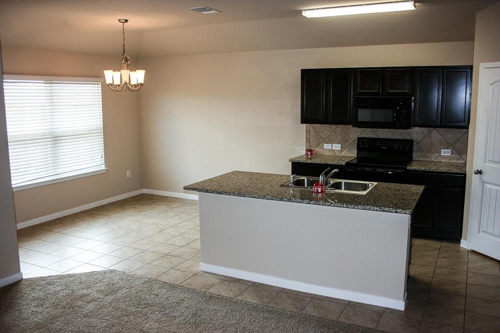 5721 Roderick Drive Austin, TX 78724 - Photo 7 of 26 Kitchen featuring black appliances, dark cabinets, backsplash, a kitchen island with sink, and light tile patterned floors
