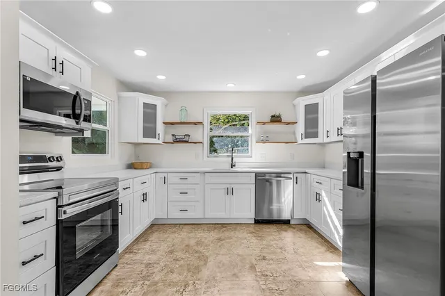 a kitchen with stainless steel appliances granite countertop a refrigerator a stove oven a sink dishwasher and white cabinets with wooden floor