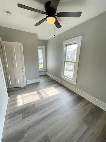 an empty room with wooden floor chandelier fan and windows