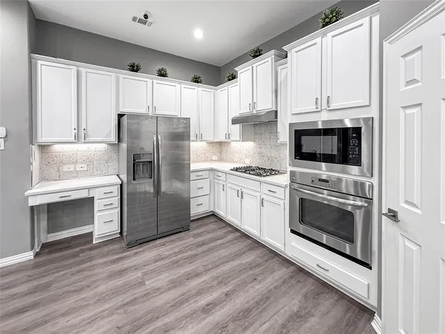 a large kitchen with a large counter top a sink stainless steel appliances and cabinets