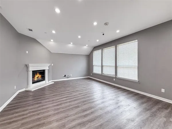 an empty room with wooden floor fire place and kitchen view
