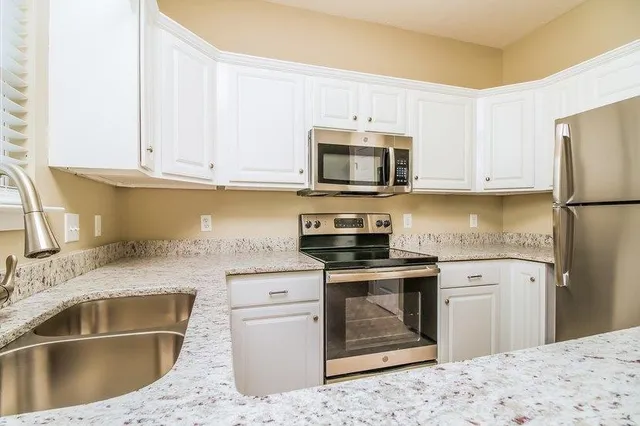 a kitchen with granite countertop a sink stainless steel appliances and white cabinets