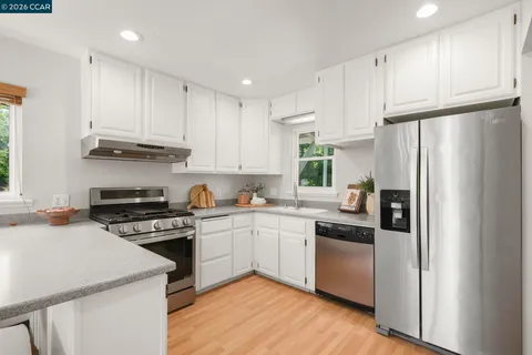 a kitchen with stainless steel appliances granite countertop a refrigerator a sink dishwasher a stove and white countertops with wooden floor