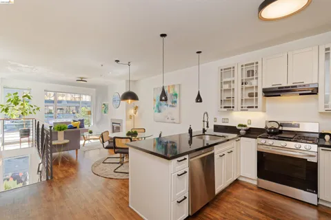 a kitchen with stainless steel appliances granite countertop a stove top oven a sink dishwasher and white cabinets with wooden floor