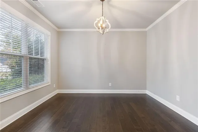 an empty room with wooden floor chandelier and windows