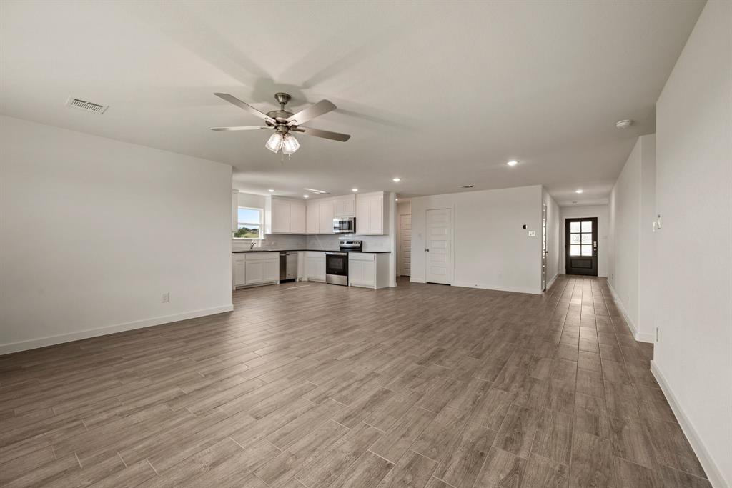 1016 Gatlin Circle Springtown, TX 76082 - Photo 10 of 30 a view of an empty room and kitchen view with wooden floor and a ceiling fan