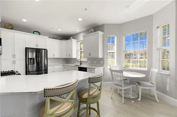 a kitchen with stainless steel appliances kitchen island granite countertop a dining table chairs and a refrigerator