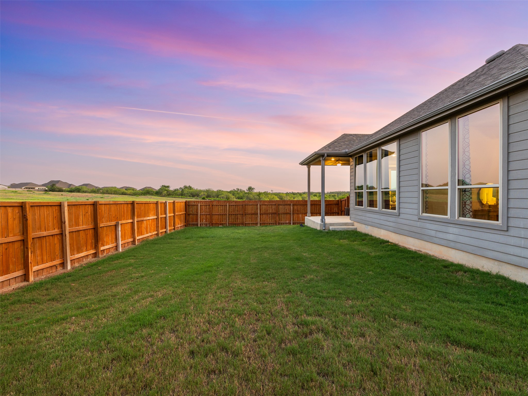606 Spinnaker Loop Kyle, TX 78640 - Photo 28 of 37 A spacious, fenced backyard offers a serene outdoor retreat under a colorful sky.