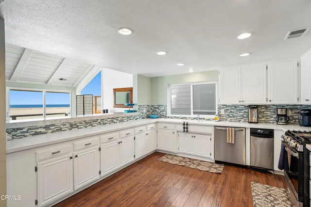 a kitchen with granite countertop a stove a sink and white cabinets with wooden floor