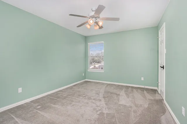 an empty room with a chandelier fan and windows