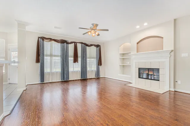 an empty room with wooden floor fireplace and windows