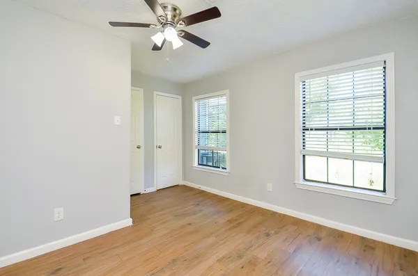 an empty room with wooden floor chandelier fan and windows