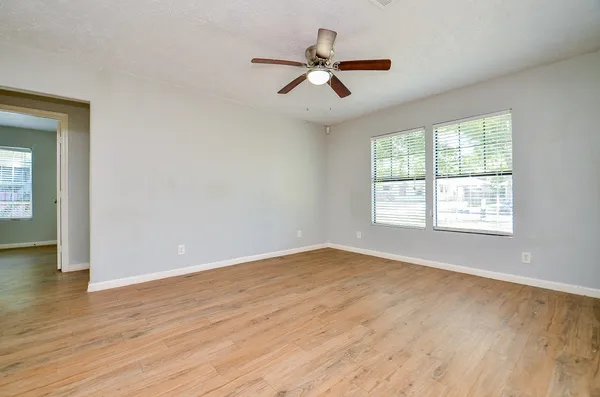 an empty room with wooden floor fan and windows