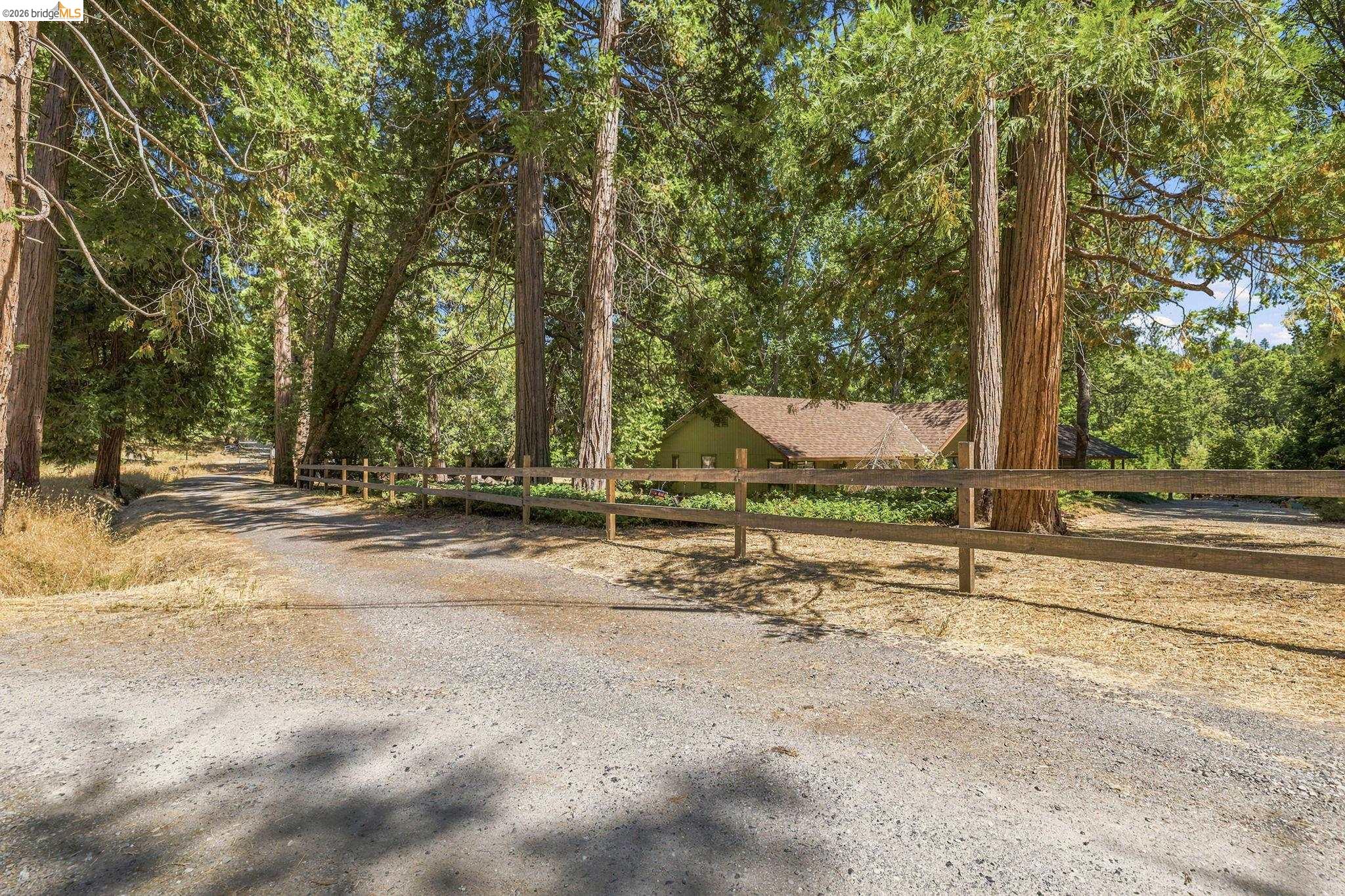 22401 South Fork Road Sonora, CA 95370 - Photo 10 of 34 Gravel driveway partially bordered by a rustic wooden fence, surrounded by mature trees