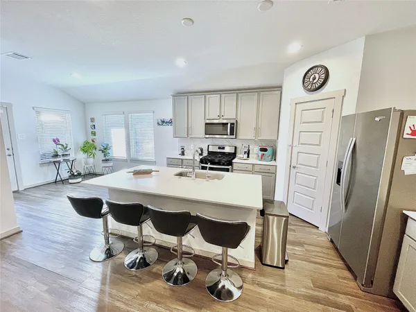 a kitchen with granite countertop a refrigerator a stove a sink and white cabinets with wooden floor