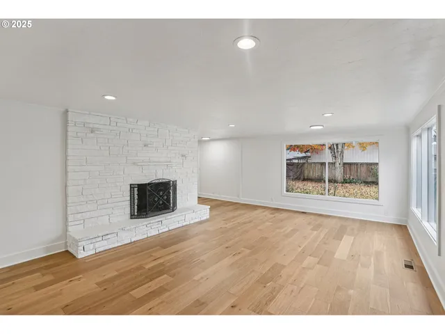 a view of an empty room with wooden floor and fan