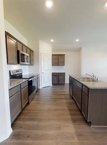 a large kitchen with stainless steel appliances granite countertop a large stove top oven a refrigerator a sink dishwasher and white cabinets with wooden floor